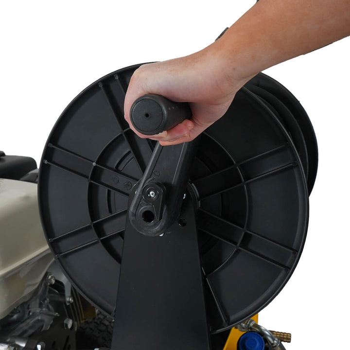 Close up of someone turning a hose reel belonging to a yellow and black pressure washer by brand Skyvac, model SlimStream Pro 20, and engine Honda.