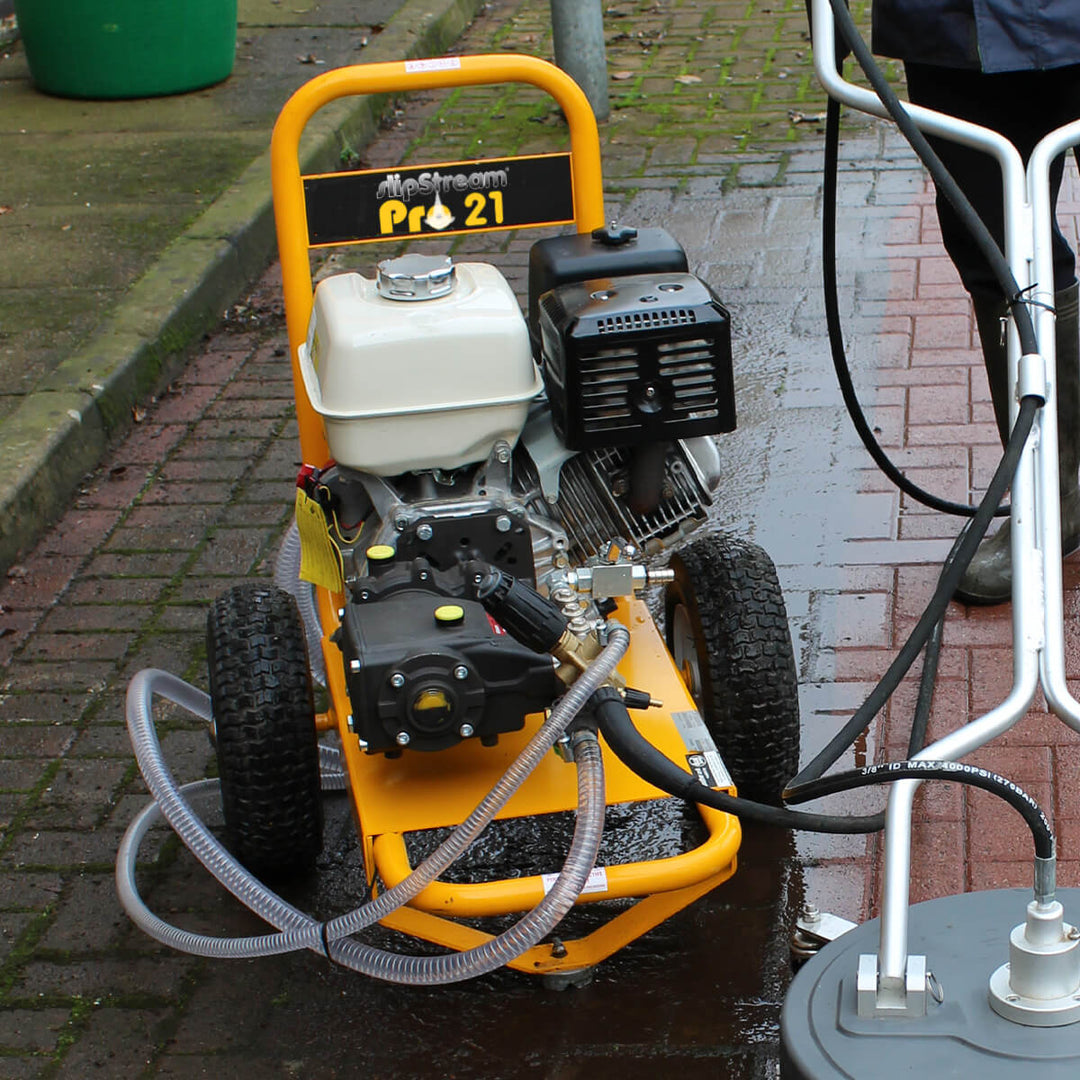 In use and on a pavement, is a yellow and black pressure washer by brand Skyvac, model SlipStream Pro 21.